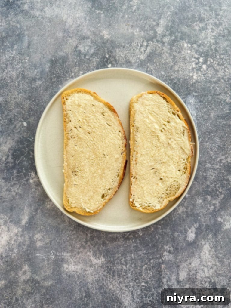 Spreading butter on a slice of sourdough bread for a grilled cheese sandwich.