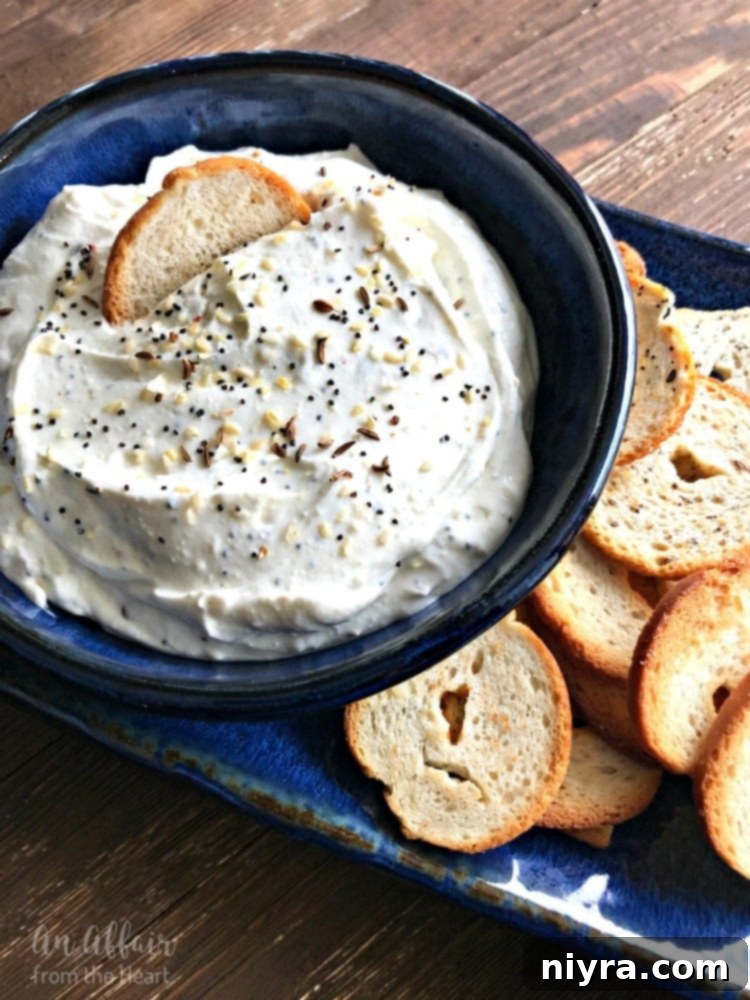 Everything Bagel Dip in a bowl with a spreader and bagel chips.