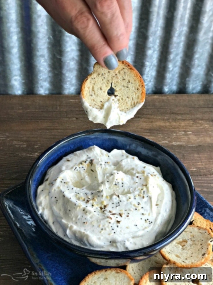 Everything Bagel Dip in a bowl with a bagel chip being dipped in.