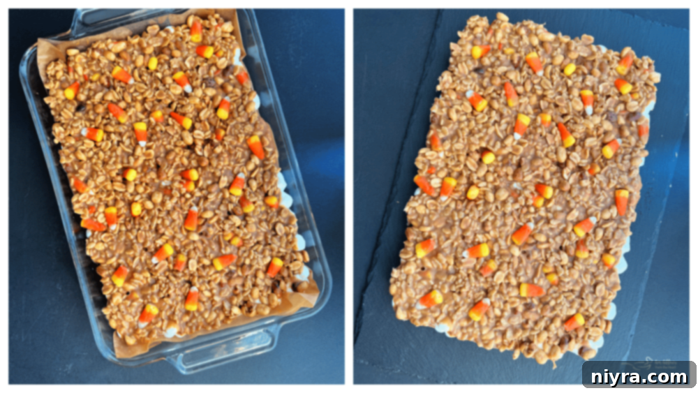 Peanut butter and candy corn topping being spread over the gooey marshmallow layer in a baking pan.