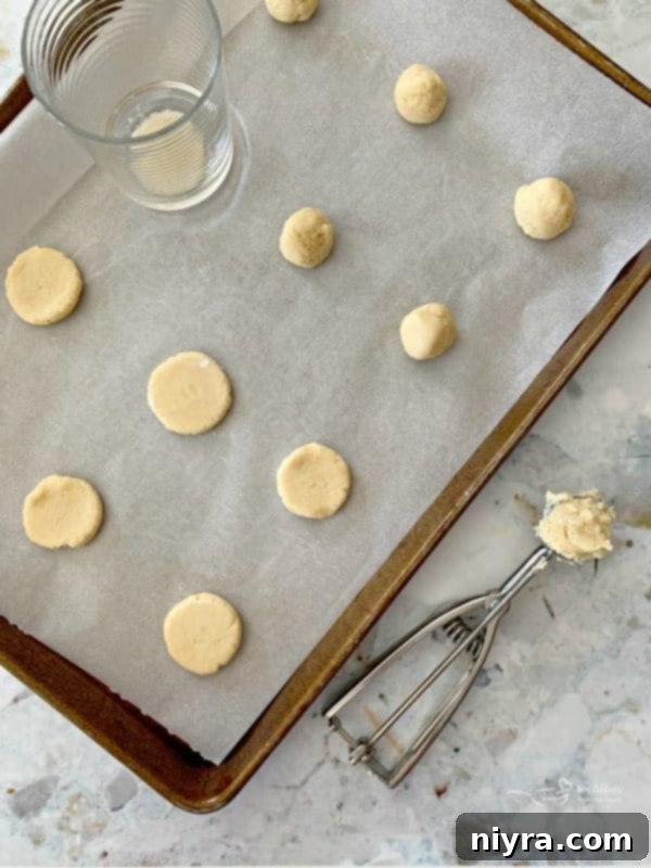 Cookie dough balls being pressed with the bottom of a glass, lightly dusted with flour