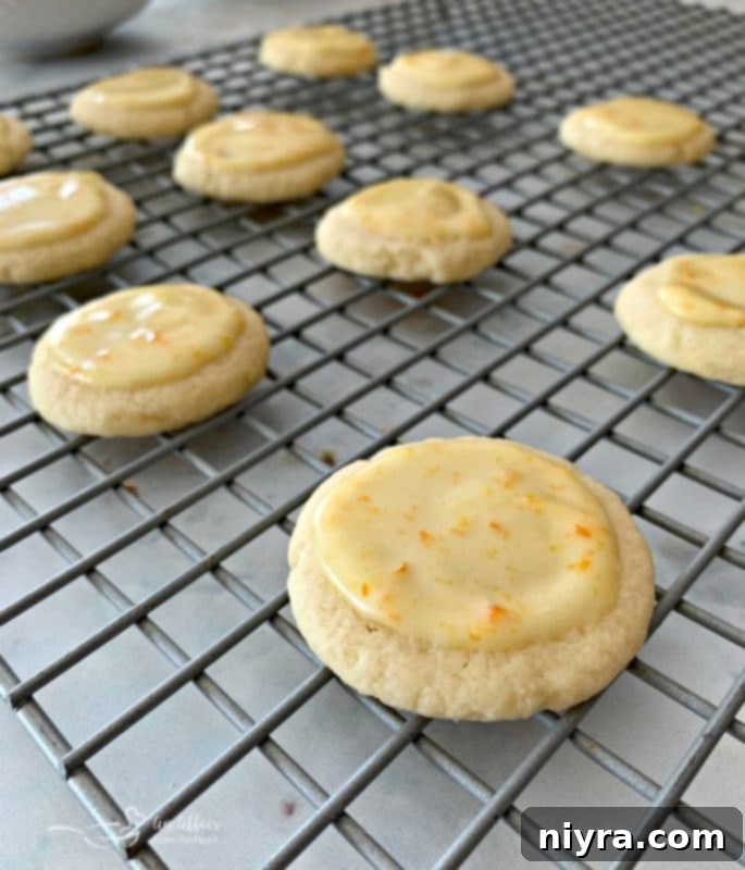Several glazed Orange Meltaway Cookies, some with a puddle of glaze, on a white plate