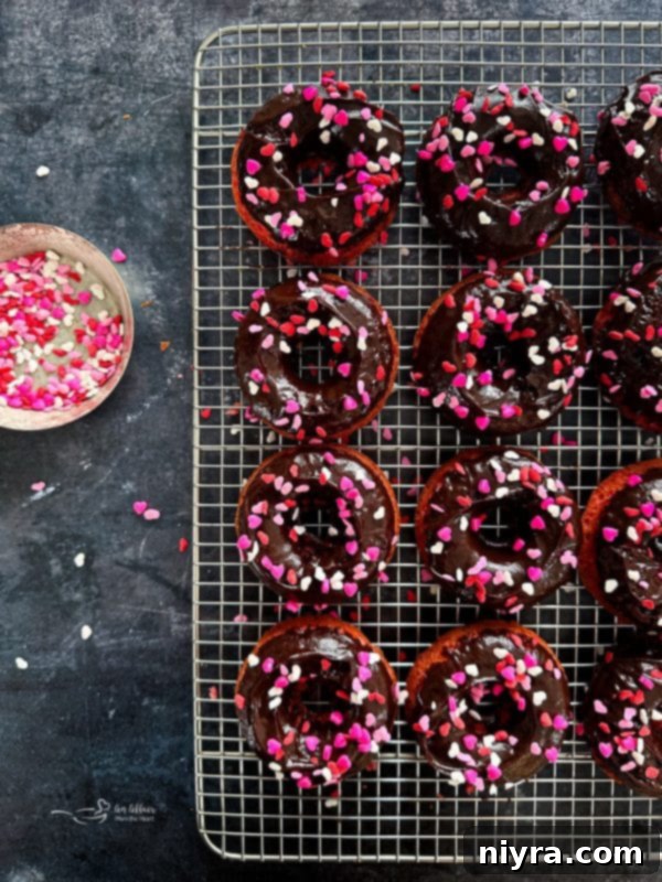 A baked strawberry donut being dipped into chocolate ganache.