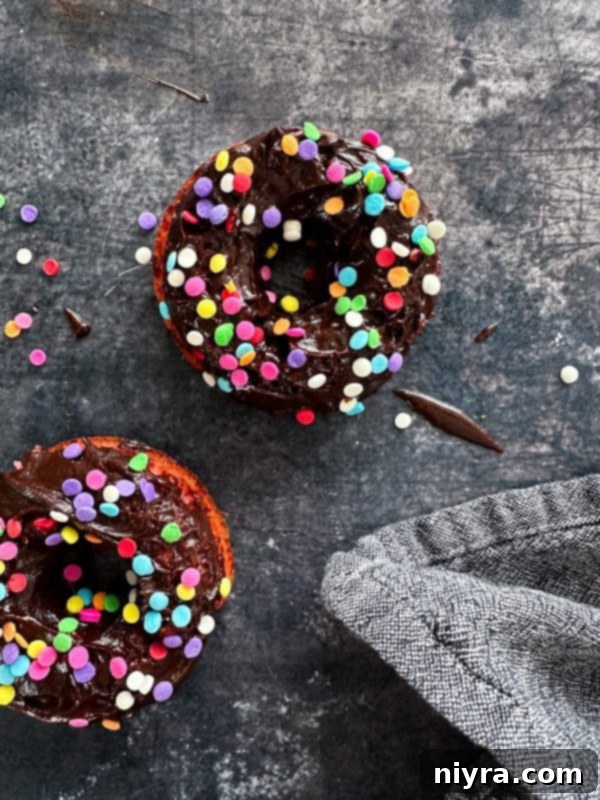 Several baked chocolate covered strawberry donuts in a heart-shaped serving dish with a rustic wooden background.