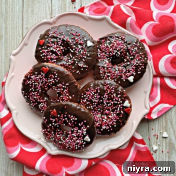 A heart-shaped baked chocolate covered strawberry donut against a rustic wooden background, perfect for Valentine's Day.