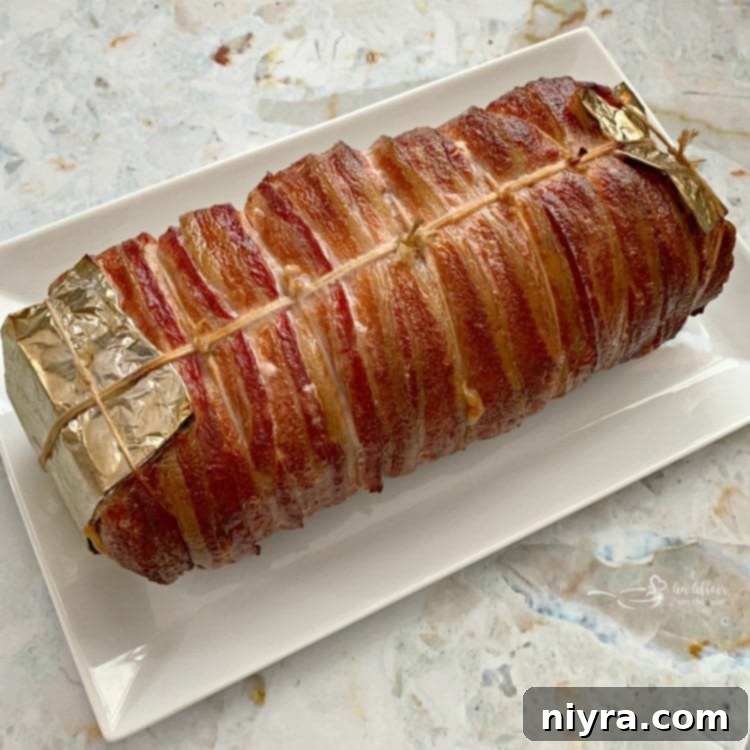 Cooked Bacon Wrapped Pork Loin with Sauerkraut Stuffing resting on a white platter.