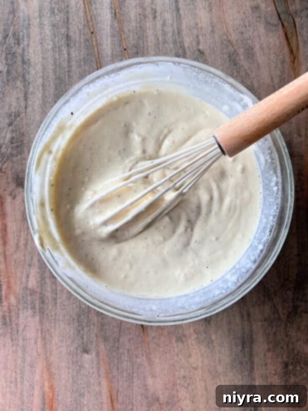 Hearty Spam Pasta Salad 6 Close-up of mayonnaise, dill pickle juice, and black pepper being whisked together for the dressing.