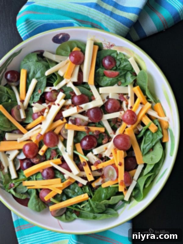Silverglade Harvest Spinach Salad 4 Fresh Silverglade Spinach Salad before dressing, showcasing vibrant spinach, halved red grapes, and julienned Swiss and Cheddar cheeses
