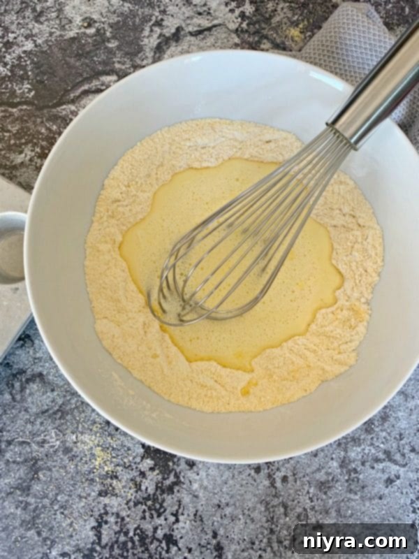 Wet ingredients being poured into a well of dry ingredients for Corn Dog Mini Muffins