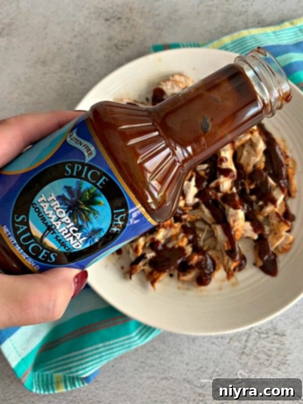 Shredded chicken tossed with Spice Isle Tropical Tamarind Sauce in a bowl, ready for building the nachos.