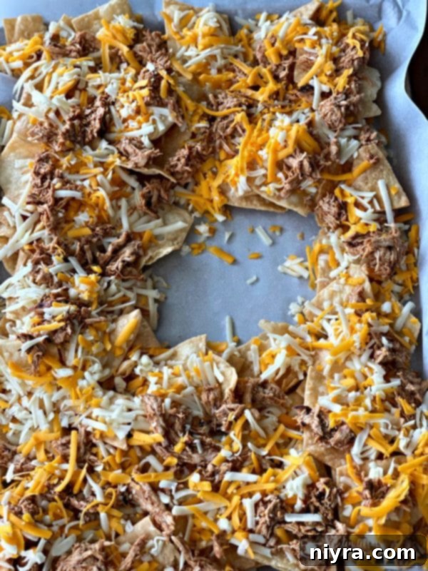 A sheet pan with tortilla chips, cheese, and seasoned chicken arranged, leaving a center space for a pineapple bowl, ready for baking.