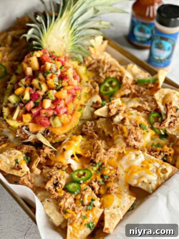 The ultimate Tropical Chicken Nachos with Tropical Salsa, beautifully presented with a pineapple bowl of salsa in the center, garnished with cilantro and jalapeños.