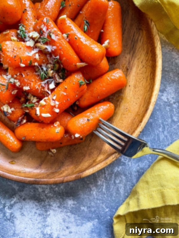Vibrant orange glazed baby carrots, perfectly cooked and glistening on a white plate, ready to be served.