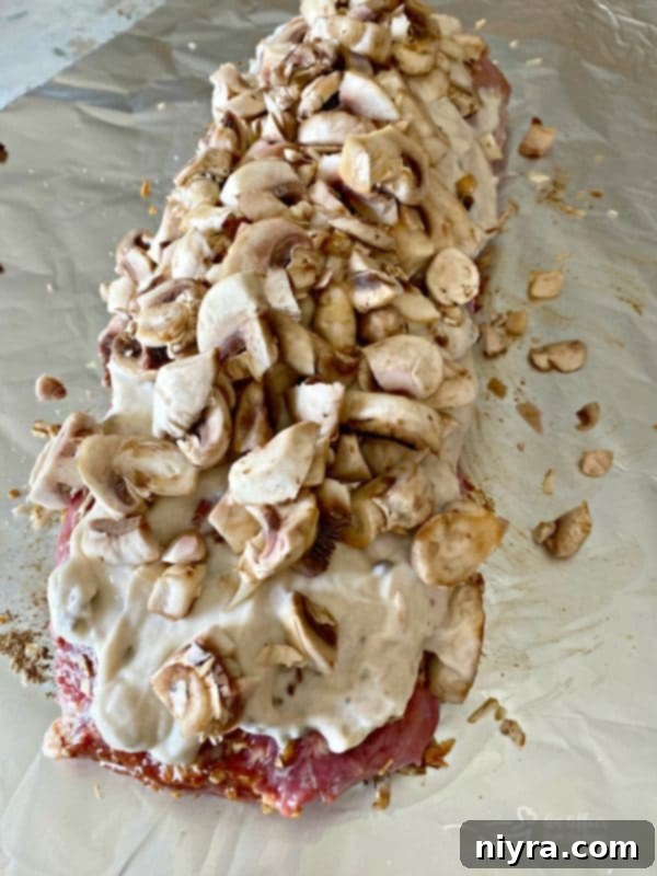 Cream of mushroom soup spread over the pork roast, with fresh mushrooms added on top, preparing for the Fuggedaboutit cooking method.