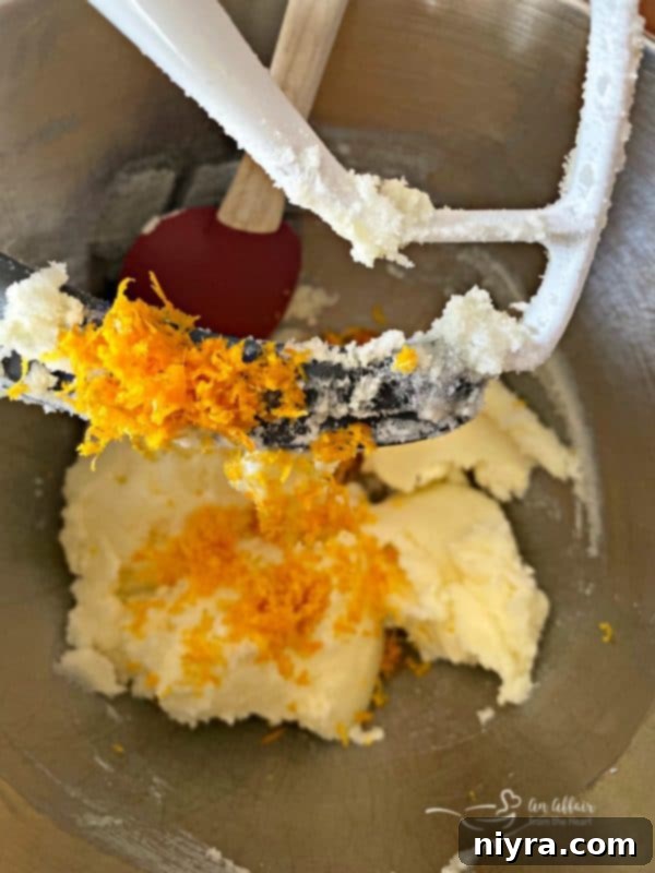 Fresh orange zest being added to creamed butter and sugar in a large mixing bowl