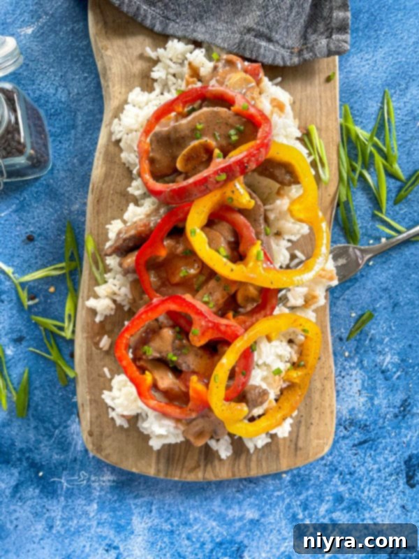 Delicious Pepper Steak served with rice and colorful bell peppers on a wooden surface.