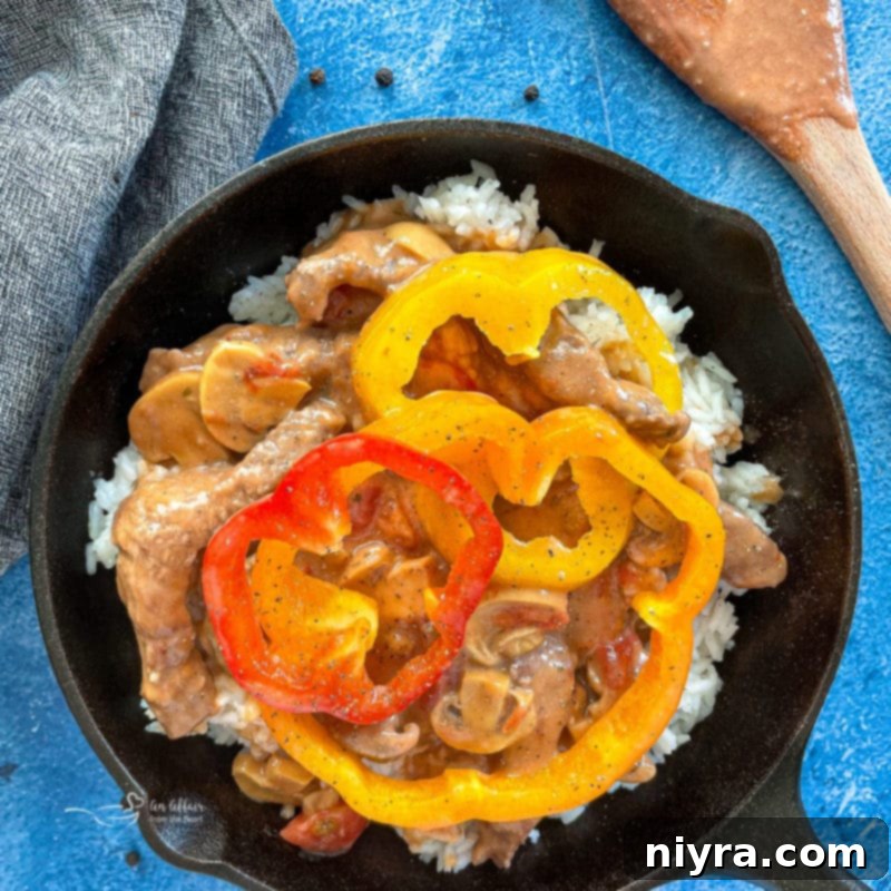Colorful bell peppers arranged on top of simmering pepper steak in a pan.