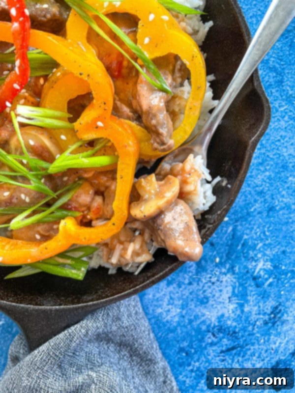 Close-up image of a generous serving of pepper steak in a pan, showing the tender meat and rich sauce.