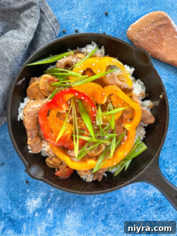Top-down view of tender pepper steak simmering in a pan with vibrant bell peppers and mushrooms.