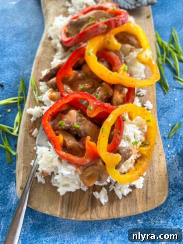 Close-up of a plate of homemade pepper steak, served with white rice and a colorful array of bell peppers.