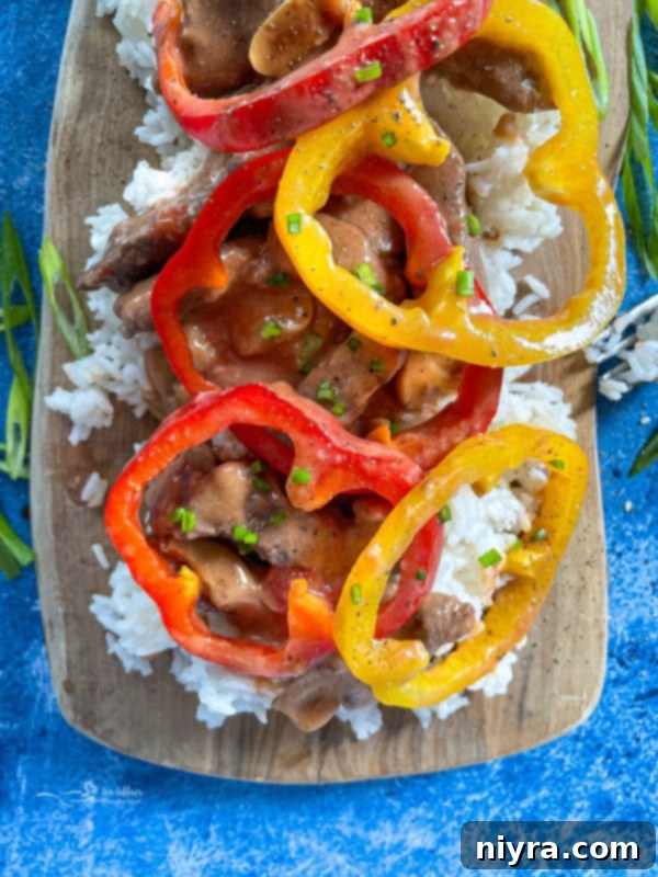 Top-down view of pepper steak in a pan, garnished with colorful bell peppers.