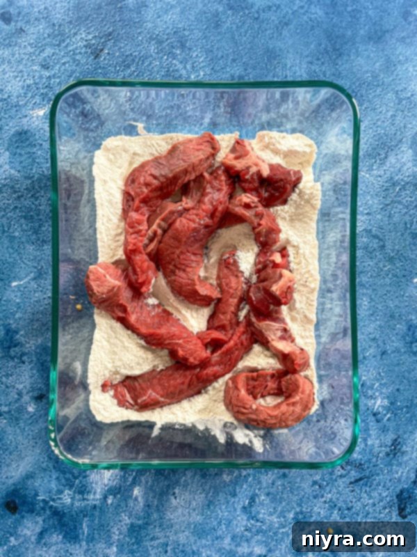 Minute steak slices being seasoned with flour, salt, and pepper.