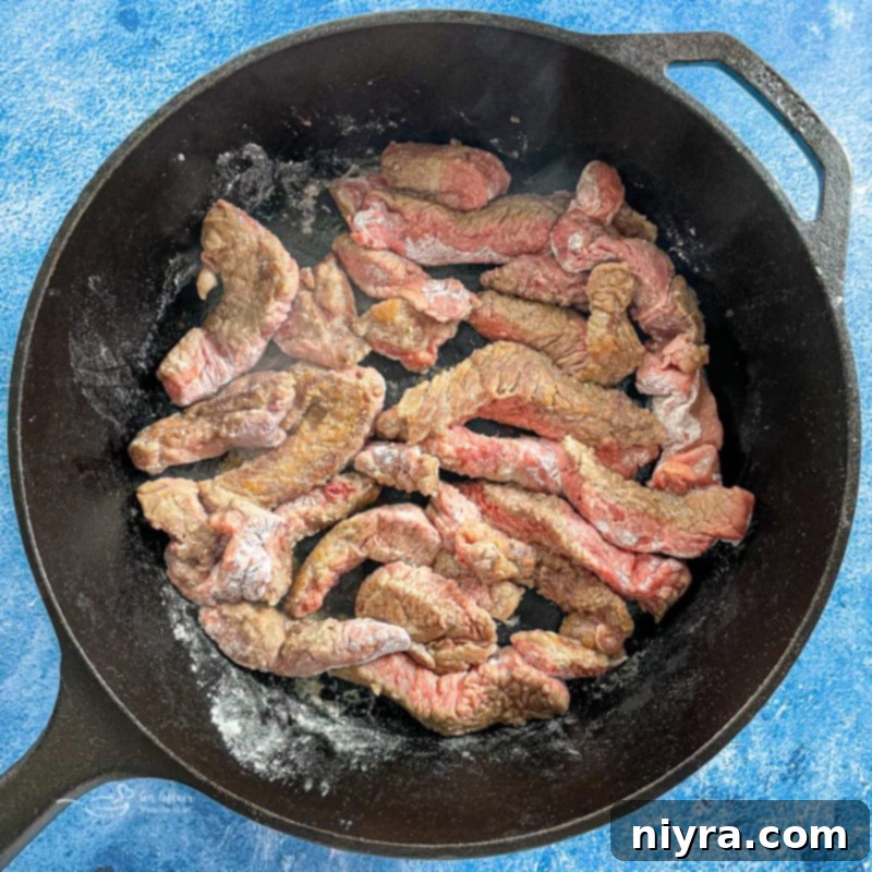 Slices of minute steak browning in a hot skillet with oil.