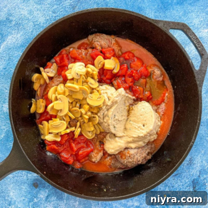 Top-down view of pepper steak simmering in a pan with the sauce ingredients.