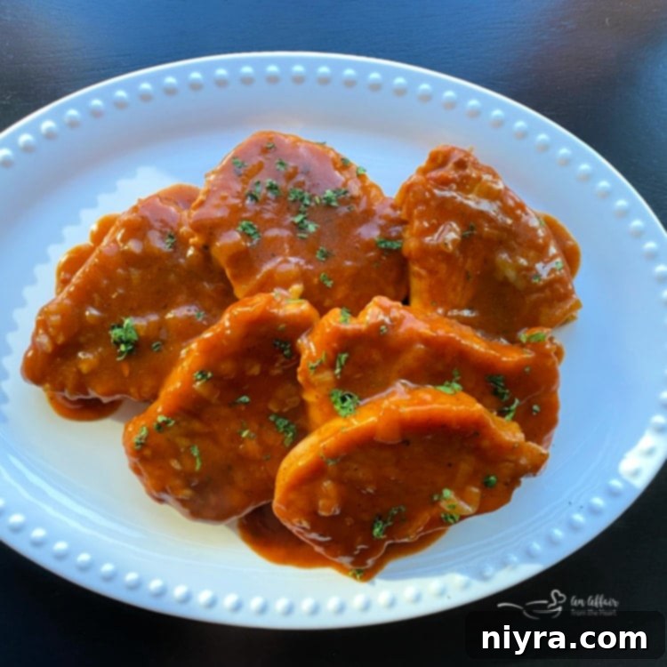 Close-up of a perfectly cooked Taco Pork Chop, tender and glistening with spicy red sauce, garnished with fresh cilantro.