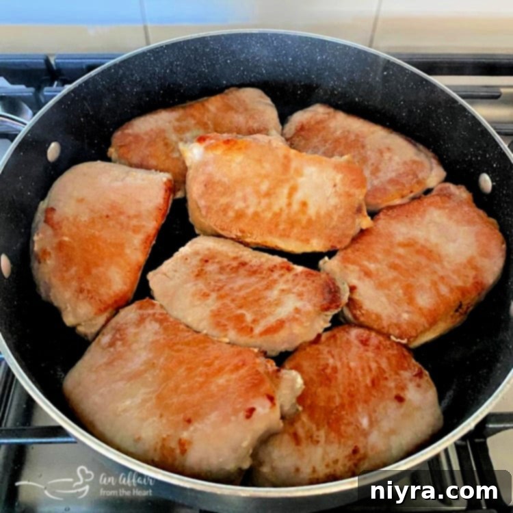 Boneless pork chops browning in a skillet with olive oil, developing a golden crust.