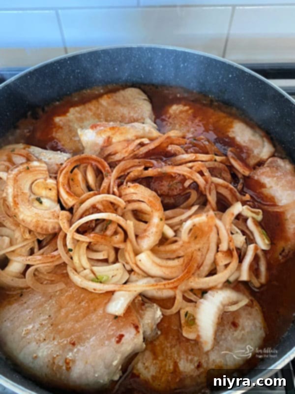 Browned pork chops in a skillet, covered with the spiced tomato and onion sauce, simmering to perfection.