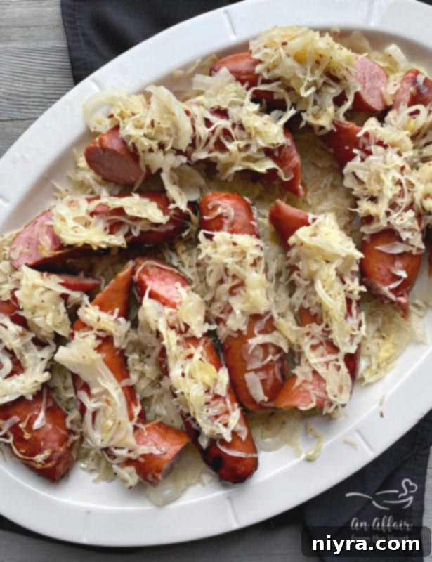 Close-up of grilled Polish sausage and sauerkraut in an aluminum pan with chopped parsley for garnish