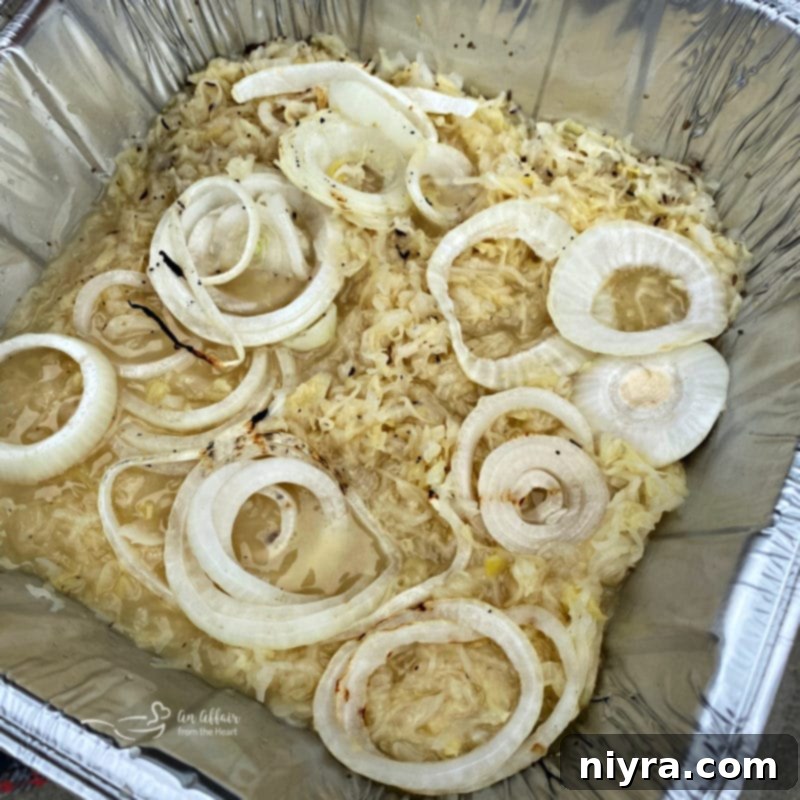 Cooked Polish sausage quarters and grilled onions nestled into a pan of sauerkraut mixture on the grill