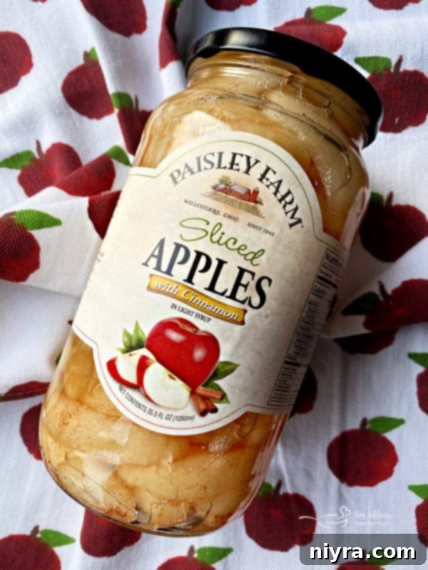 Close-up of baked Apple Bars in a pan, showcasing golden crust and apple filling, with Paisley Farm jar in background