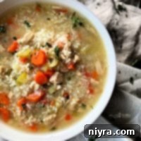 Hearty Instant Pot Chicken and Rice Soup 10 Close up of Instant Pot Chicken & Rice Soup in a white bowl, garnished with fresh herbs