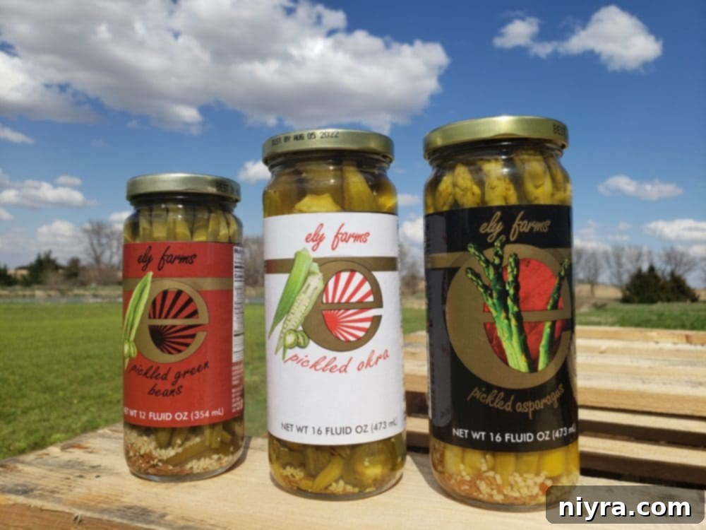 Three jars of Ely Farms pickled vegetables: asparagus, green beans, and okra, neatly arranged to highlight their natural and artisanal quality, suggesting a range of delicious products.