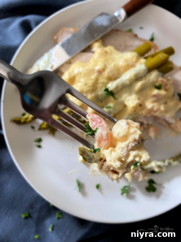 A close-up shot of a single serving of Turkey Oscar, highlighting the layers of tender turkey, vibrant asparagus, and a generous topping of creamy Hollandaise sauce with visible pieces of succulent shrimp and delicate crab, ready for a delicious bite.
