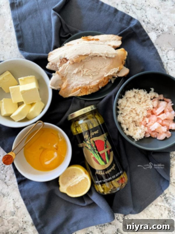 A flat lay image displaying all the fresh ingredients for Turkey Oscar, including sliced cooked turkey breast, a jar of pickled asparagus, raw shrimp, canned crabmeat, eggs, a lemon, and butter, neatly arranged and ready for preparation.