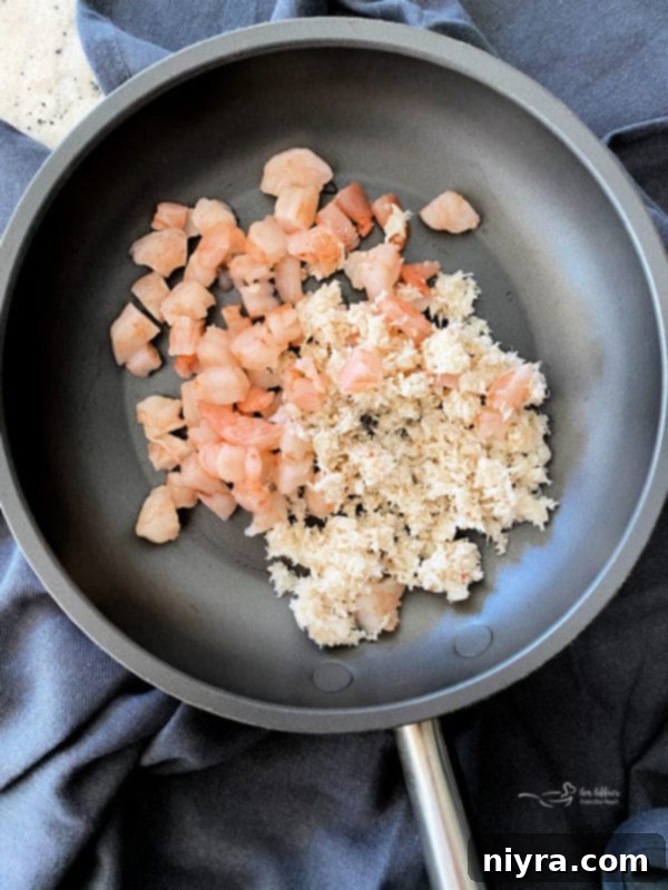 Close-up of a small skillet on a stove, containing cooked shrimp and drained crabmeat gently warming, ready to be combined with the Hollandaise sauce for the Turkey Oscar dish.