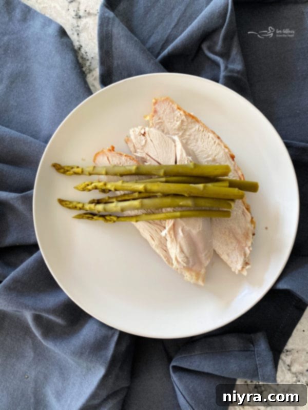 Warm slices of turkey breast neatly arranged on a white plate, elegantly topped with several bright green spears of Ely Farms Pickled Asparagus, poised for the next step of sauce application and final presentation.
