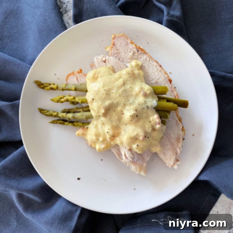 A beautifully plated Turkey Oscar dish, showcasing the tender turkey and asparagus beneath a generous helping of creamy Hollandaise sauce, studded with succulent shrimp and delicate crabmeat, and garnished with fresh black pepper, ready to be served.