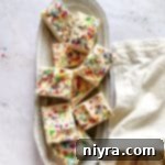 Frosted sugar cookie bars stacked on a white serving plate.