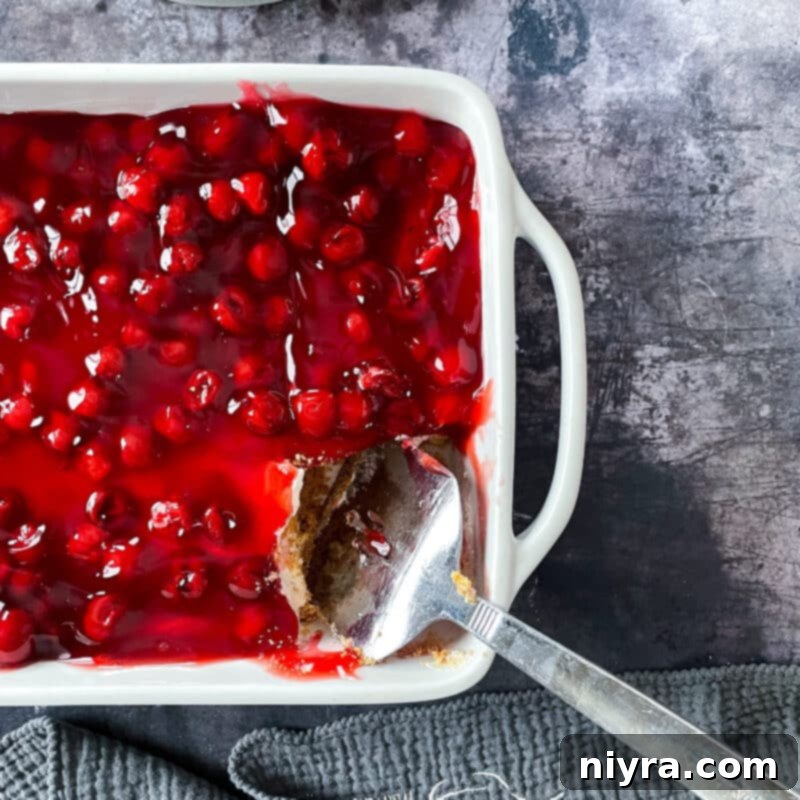 Crimson Cherry Indulgence 16 A wide shot of the assembled cherry dessert in a rectangular pan with a spoon scooping a portion.