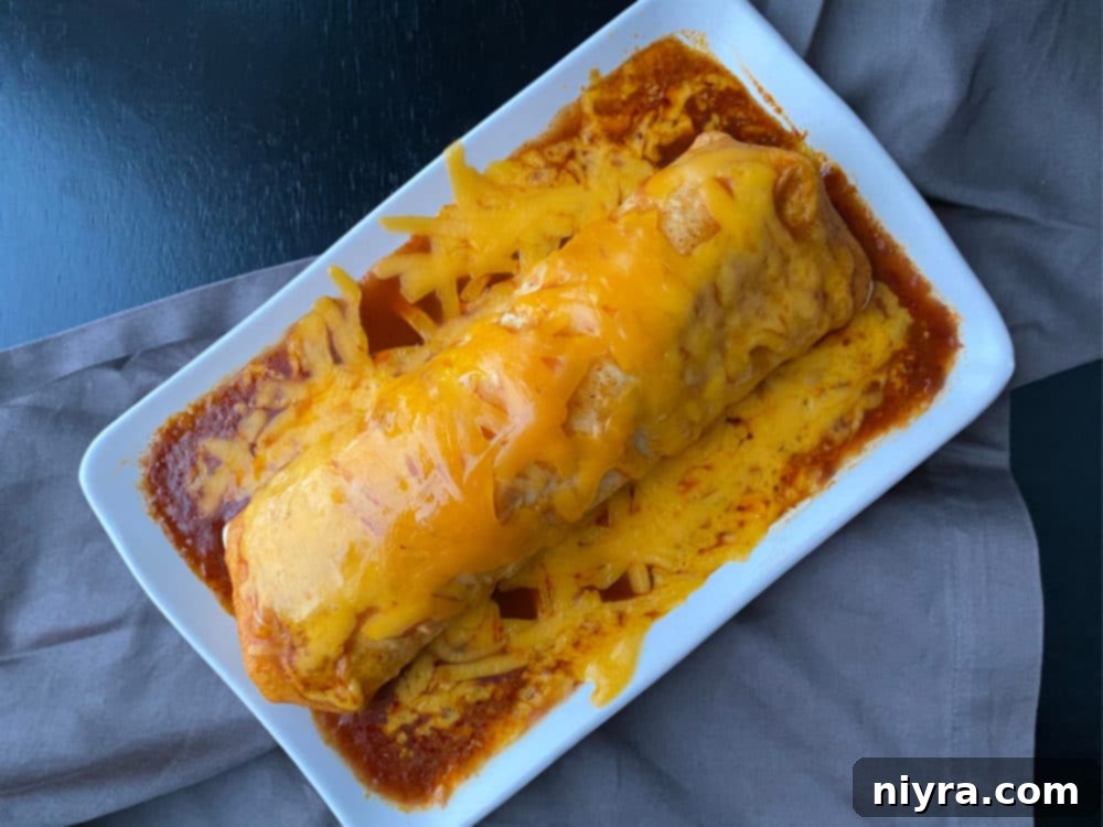 A rolled Enchirito, generously covered in red enchilada sauce and shredded cheese, ready to be heated until the cheese is perfectly melted.