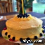 Lemon Blueberry Burst Cake 2 Overhead shot of a beautifully decorated Lemonade Cake with Blueberry Filling and Lemonade Buttercream frosting, featuring a single birthday candle.