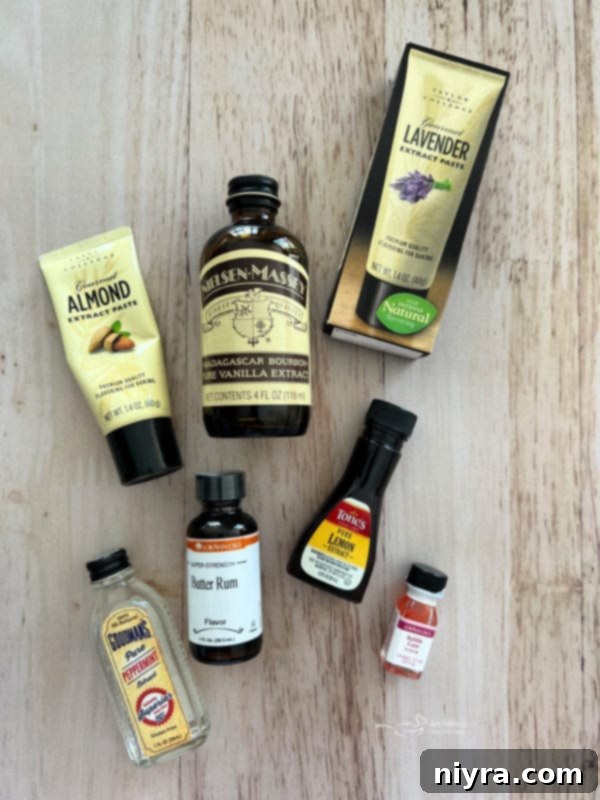 An overhead shot of various small bottles of extracts laid out on a surface, including vanilla, almond, lemon, and others, with granulated sugar in a bowl in the background.