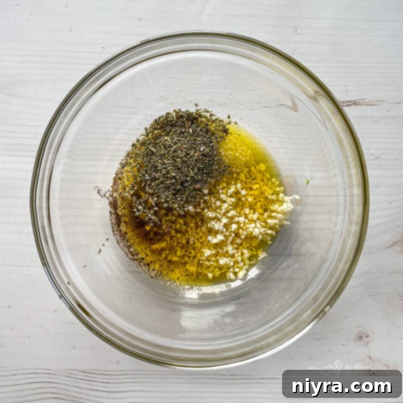 Top view of garlic, olive oil, and seasoning in clear bowl