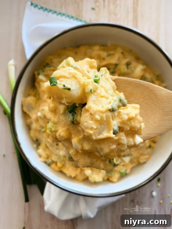 A chef's knife dicing hard-boiled eggs on a wooden cutting board, with potatoes, celery, and green onions nearby.