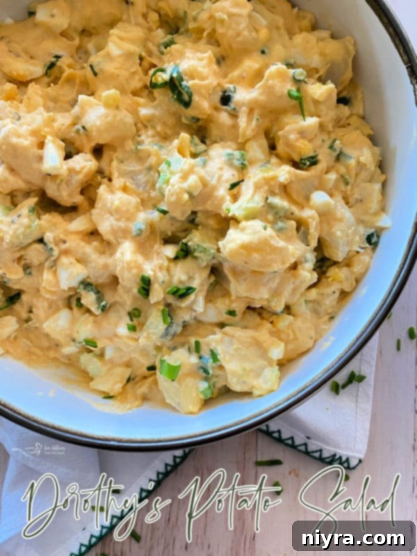 A large bowl of Dorothy's Potato Salad with a serving spoon, garnished with fresh herbs, ready for a gathering.
