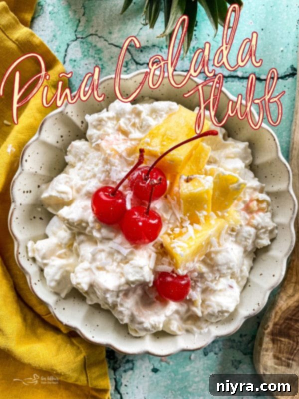 A vibrant bowl of Piña Colada Fluff dessert salad, garnished with a cherry and mint leaf.